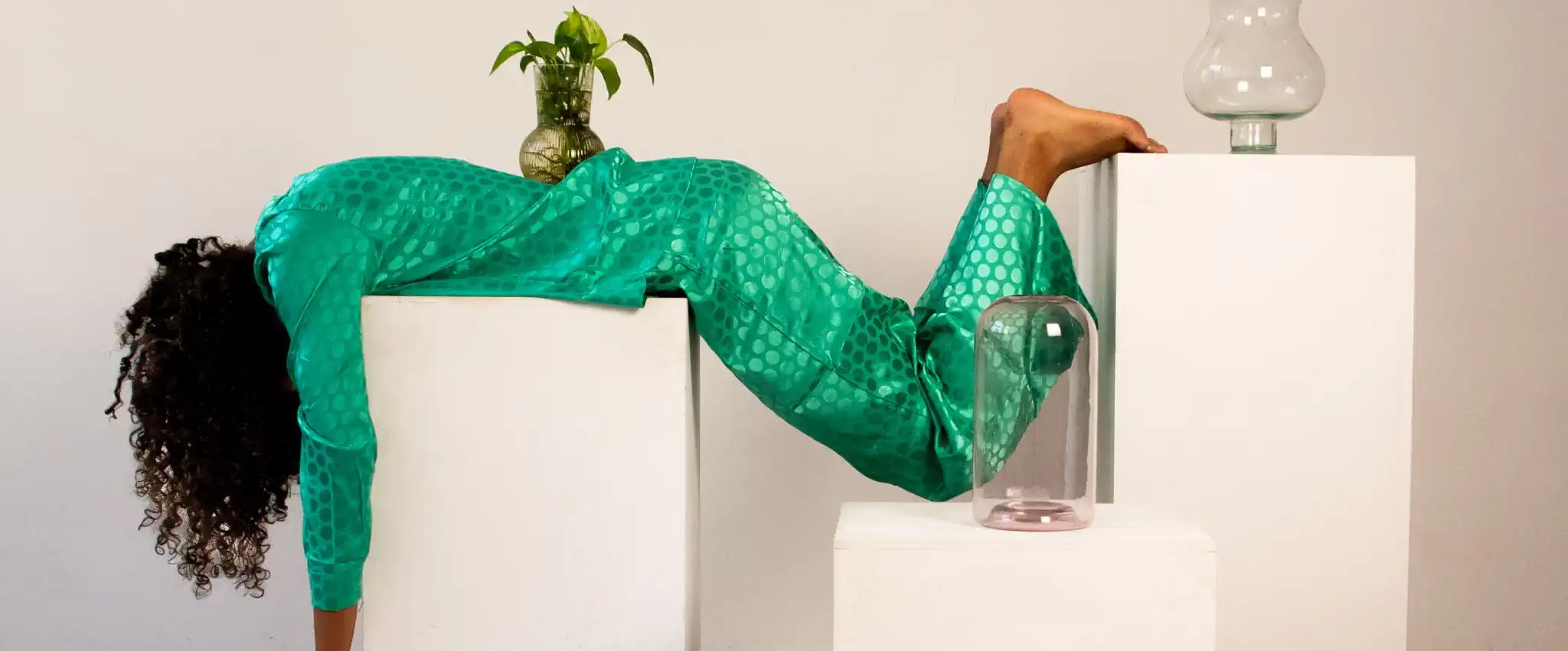 Yeşil kıyafetli kadın iki beyaz kaide arasında askıda — anksiyete ve zihinsel gerilimin beden üzerindeki etkisini simgeleyen yaratıcı yoga görseli.